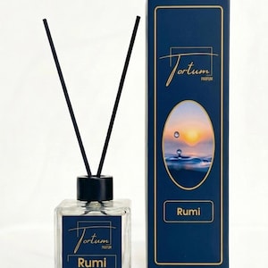 May include: A square glass bottle with black reeds and a matching black cap, next to a navy blue box. The bottle and box feature the text "Jortum Parfum" and "Rumi". The box has a sunset image.