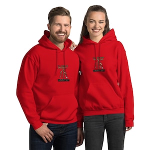 May include: Two people wearing matching red hoodies. Each hoodie has a front pocket and a hood. The hoodies feature a Christmas-themed graphic with text that reads "All I want for Christmas is..." and a list of items.