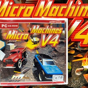 May include: A PC CD-ROM game case for Micro Machines V4. The cover features a red truck and a blue car racing. The game title is in yellow and red, with the number 4 prominently displayed. The case is in a clear plastic case.