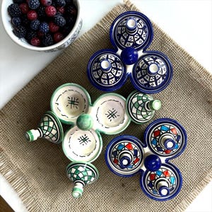Peut inclure: Trois services à condiments en céramique composés de trois bols reliés et de couvercles coniques assortis. Un service présente des motifs géométriques bleu et blanc, un autre des carreaux vert et blanc, et le troisième des motifs triangulaires rouge, bleu et blanc.