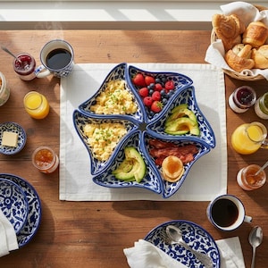 Peut inclure: Un plat de service en céramique en forme d'étoile à six sections, orné d'un motif floral bleu et blanc. Le plat est rempli d'aliments pour le petit-déjeuner, notamment des œufs brouillés, de l'avocat tranché, du bacon, des mini-crêpes, des fraises et des myrtilles.
