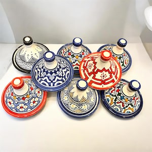 May include: A collection of seven ceramic tagine lids featuring various hand-painted geometric and floral patterns in vibrant colours including red, blue, green, yellow, and black. Each conical lid has a small knob handle at the top.