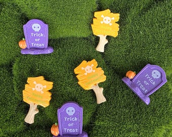 May include: A collection of miniature Halloween decorations including three purple tombstones with a skull icon and the text Trick or Treat, and three orange wooden-style signs with a skull icon and the text Happy Halloween.