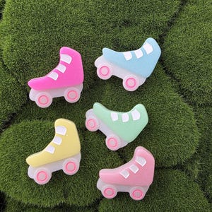 May include: Five colourful roller skate charms in pink, blue, yellow, and green with white and pink accents. The charms are arranged on a bed of green moss. These charms are ideal for crafting and jewellery making.