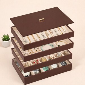 May include: A dark brown, multi-tiered jewelry organizer box with a removable lid featuring a small gold handle. The stackable trays are lined with beige fabric and contain various necklaces, rings, bracelets, and wristwatches in compartments.