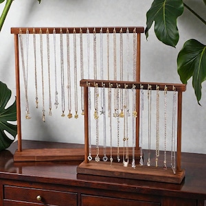 May include: Two wooden jewelry display stands with multiple necklaces hanging from them. The stands are made of dark brown wood and have a rectangular base. The necklaces are of varying lengths and feature different pendants, including keys, stars, and geometric shapes.
