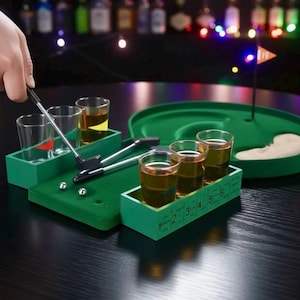 Może przedstawiać: Zielony zestaw do gry w miniaturowego golfa z kieliszkami. Zestaw zawiera green, uchwyty na kieliszki, miniaturowe kije golfowe i kieliszki wypełnione złotym płynem. Ręka trzyma kij golfowy nad zestawem.