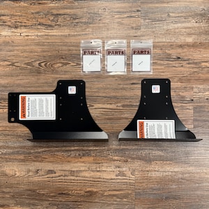 May include: Two black metal mounting brackets with pre-drilled holes and warning labels that read WARNING READ BEFORE USE. Three small clear plastic bags labeled PARTS are included, each containing hardware components for installation.