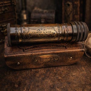Könnte beinhalten: Ein antikes Messing-Teleskop mit der Aufschrift "GILBERT & SONS" und einem Lederetui. Das Teleskop ist zylindrisch mit dekorativen Gravuren. Das Lederetui hat einen geprägten Text und eine dunkelbraune Oberfläche.