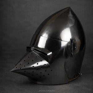 May include: A polished dark steel houndskull bascinet helmet featuring a pointed visor with multiple ventilation holes and horizontal eye slits. The metal surface is reflective and smooth, with a hinge mechanism visible on the side. Text reads primecraftsgifts.