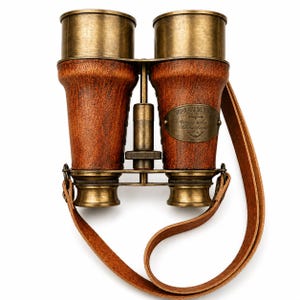 May include: Antique-style brass and brown leather binoculars featuring a central focus adjustment knob and a leather neck strap. A brass plaque on the right barrel is engraved with the text Victorian Marine Binoculars, Wotting & Co, Ealing, London, 1915.
