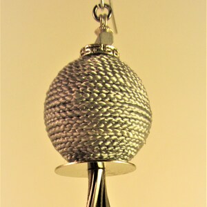 May include: Silver-toned earring with a woven sphere, a disc, and a tassel. The sphere is textured, and the tassel hangs below a decorative metal base. The earring hangs from a silver hook.