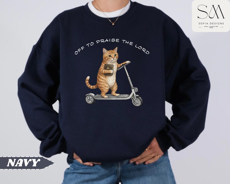 Puede incluir: Sudadera azul marino con un gato atigrado naranja montado en un patinete y sosteniendo un libro. El texto "OFF TO PRAISE THE LORD" est&aacute; arqueado sobre el gato. La palabra "NAVY" est&aacute; en la parte inferior izquierda.
