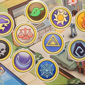May include: A collection of nine circular stickers featuring distinct icons with gold borders. The designs include a green leaf, a yellow sun, an orange flame, a purple lightning bolt, red scales, a blue eye in a triangle, a skull, a crescent moon, and a blue geometric star.