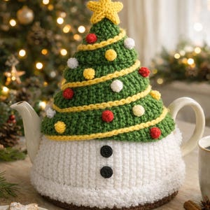 Peut inclure: Une théière en céramique blanche ornée d'un cache-théière en tricot en forme de sapin de Noël. L'arbre vert est décoré d'accents jaunes, rouges et blancs, surmonté d'une étoile jaune. La base du cache-théière ressemble à un bonhomme de neige.