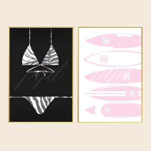 May include: Two framed wall art prints. The left print features a black background with a white zebra-striped bikini. The right print features a white background with five light pink surfboards, each displaying a white interlocking CC logo.