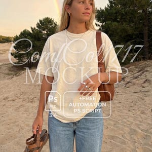 Peut inclure: Une personne porte un t-shirt crème et un jean bleu clair sur une plage de sable, tenant des sandales marron. Un sac en cuir marron est sur l'épaule. Le texte "ComfCol 717 MOCKUP" est visible sur le t-shirt. Un arc-en-ciel est en arrière-plan.