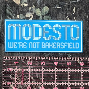 May include: A blue and white sticker with the text "MODESTO WE'RE NOT BAKERSFIELD" in a retro font.