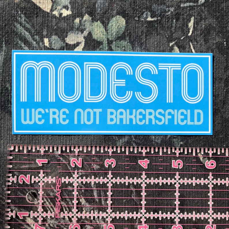 May include: A blue and white sticker with the text "MODESTO WE'RE NOT BAKERSFIELD" in a retro font.