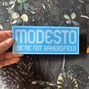 May include: A blue and white sticker with the text "MODESTO WE'RE NOT BAKERSFIELD" in a retro font.