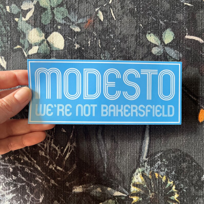 May include: A blue and white sticker with the text "MODESTO WE'RE NOT BAKERSFIELD" in a retro font.
