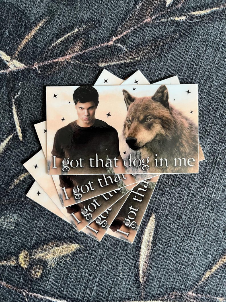 Op de afbeelding: Een stapel rechthoekige kaarten met een man en een wolf met de tekst "I got that dog in me". De kaarten hebben een lichte achtergrond met zwarte steraccenten. De achtergrond is een donkere, bedrukte stof.