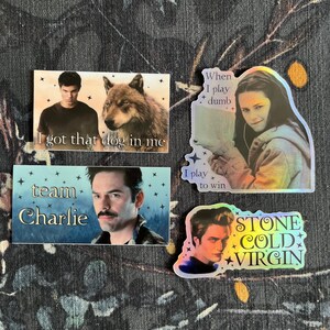 Op de afbeelding: Vier stickers met afbeeldingen en tekst. E&eacute;n toont een man en een wolf met de tekst "I got that dog in me." Een andere zegt "When I play dumb, I play to win." Een derde zegt "team Charlie." De laatste zegt "STONE COLD VIRGIN."