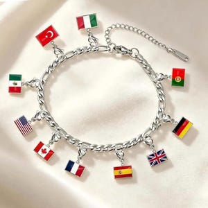 Könnte beinhalten: Ein silberfarbenes Charm-Armband mit rechteckigen Anhängern, die die Flaggen verschiedener Länder zeigen. Zu den Flaggen gehören die der Vereinigten Staaten, Kanadas, Frankreichs, Spaniens, Großbritanniens, Deutschlands, Mexikos, der Türkei, Italiens und Portugals.
