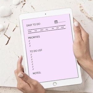 Puede incluir: Una tableta que muestra una plantilla de planificador diario digital sobre un fondo morado claro. La pantalla presenta el texto DAILY TO DO, un icono de calendario, los días de la semana y secciones etiquetadas PRIORITIES, TO DO LIST y NOTES.