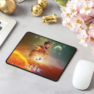 May include: Square mousepad featuring a sci-fi themed design with a man in a spacesuit, a planet, and the text "BELIEVE IN THE HAIL MARY". The background has a gradient of orange, yellow, and green.
