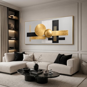 May include: A rectangular wall art piece featuring a white background with black horizontal bars, vertical gold lines, a large flat gold circle, and a smaller textured gold sphere, all framed in a thin gold border mounted on a wall.
