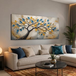 Op de afbeelding: Een groot rechthoekig wandkunstwerk met een getextureerd schilderij van een boom met een donkere stam en takken. De boom is versierd met talloze individuele bladeren in tinten heldergeel, diepblauw en wit tegen een neutrale achtergrond.