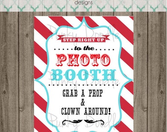 May include: A white sign with red and blue stripes. The sign says "Step Right Up to the Photo Booth. Grab a Prop & Clown Around!"