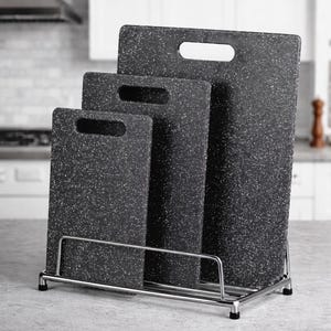 May include: A set of three dark gray cutting boards with white speckles, each with a handle cutout. The boards are displayed in a chrome wire rack, offering a space-saving storage solution for the kitchen.