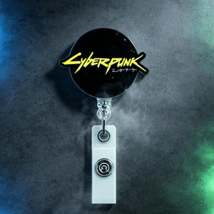 May include: A black and yellow Cyberpunk 2077 retractable badge reel. The reel has a black circular design with the words "Cyberpunk 2077" in yellow. The badge holder is white and has a silver-colored metal clip.