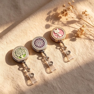 May include: Three circular metal badge reels with clear plastic straps and snap buttons. The left reel features a green tree design, the center reel has a purple mandala pattern, and the right reel displays a pink cat silhouette, all with crystal-studded borders.