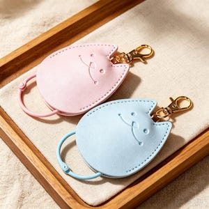 以下が含まれることがあります： パステルピンクとライトブルーの猫型キーカバー2点。それぞれに猫の顔が型押しされており、ゴールドのナスカンと、鍵を収納するための同色の丸いリングが下端に取り付けられています。