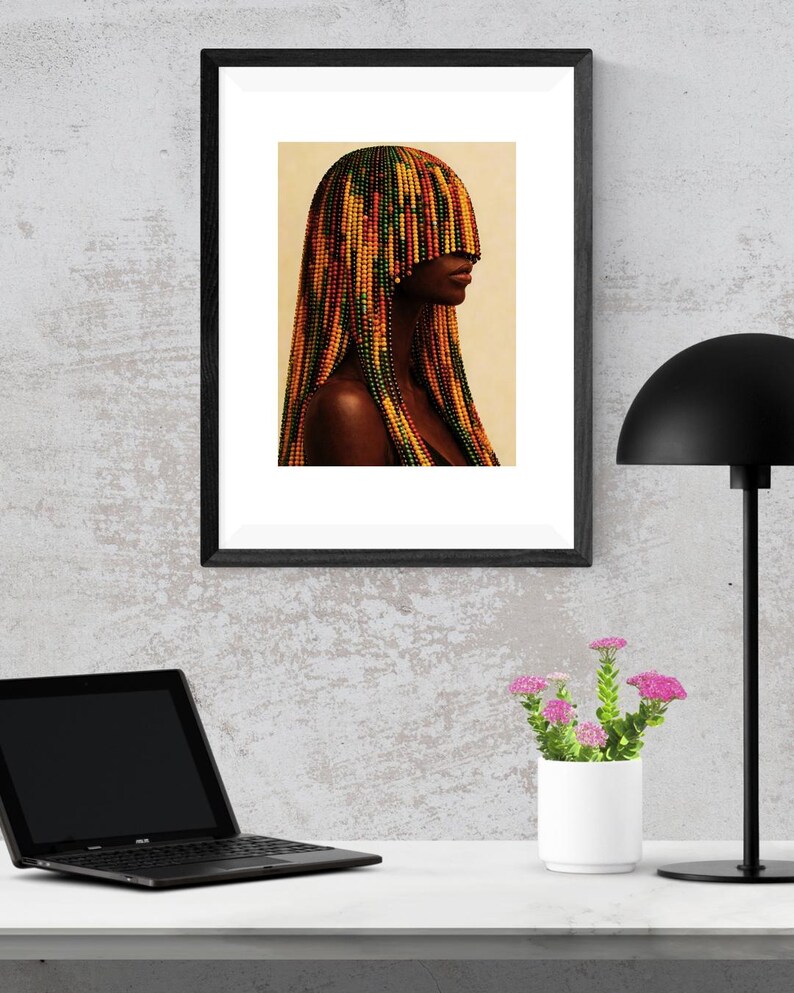K&ouml;nnte beinhalten: Gerahmter Kunstdruck mit einem Portr&auml;t einer Person mit einer farbenfrohen Perlenfrisur. Das Kunstwerk befindet sich in einem schwarzen Rahmen und wird auf einer wei&szlig;en Oberfl&auml;che mit einem Laptop, einer kleinen wei&szlig;en Vase mit rosa Blumen und einer schwarzen Schreibtischlampe pr&auml;sentiert.