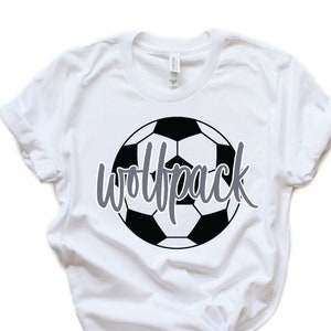 Puede incluir: Camiseta blanca con un gráfico de balón de fútbol blanco y negro y el texto "Wolfpack" en gris.
