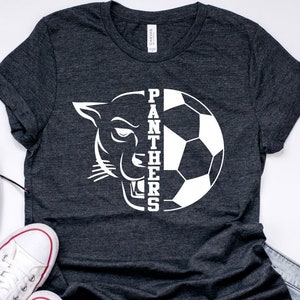 May include: A dark gray t-shirt with a white graphic of a panther's head and a soccer ball with the word "PANTHERS" written vertically down the side.