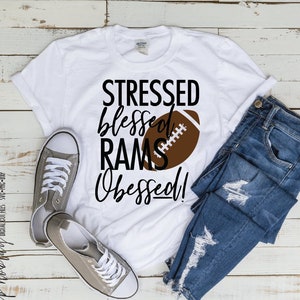 Peut inclure: T-shirt blanc avec du texte noir qui dit "Stressed Blessed Rams Obsessed!" et un graphique de ballon de football brun.