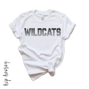 May include: White t-shirt with black text that reads "WILDCATS" in a striped font.