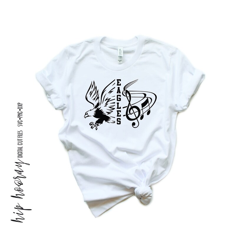 May include: White t-shirt with a black design of an eagle and musical notes. The text "EAGLES" is vertically oriented on the right side of the design.