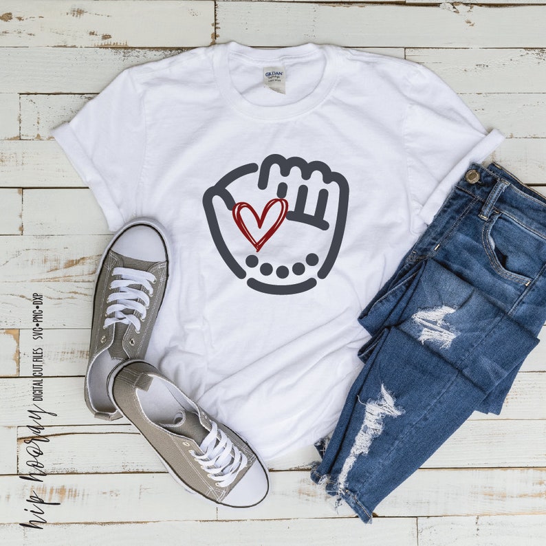 K&ouml;nnte beinhalten: Wei&szlig;es T-Shirt mit einem grauen Baseballhandschuh-Motiv und einem roten Herzen darin. Das Shirt liegt auf einer Holzoberfl&auml;che mit einem Paar grauer Turnschuhe und einer blauen Jeans.