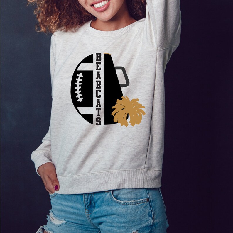 Op de afbeelding: Een grijs sweatshirt met een zwart en gouden ontwerp. Het ontwerp bevat een voetbal, een megafoon en de woorden "BEARCATS".