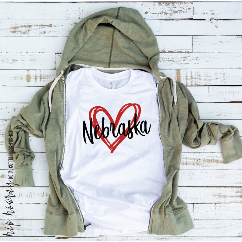 Peut inclure: T-shirt blanc avec un c&oelig;ur rouge et le mot "Nebraska" en noir. Le t-shirt est pr&eacute;sent&eacute; sur un sweat &agrave; capuche vert zipp&eacute;. Le fond est constitu&eacute; de planches de bois blanches. Fichier de d&eacute;coupe num&eacute;rique.