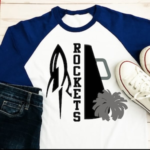 May include: White and blue baseball t-shirt with a black rocket and megaphone graphic and the word "ROCKETS" in black text.