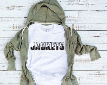 Op de afbeelding: Wit T-shirt met het woord "JACKETS" bedrukt in zwarte blokletters. Het shirt is gevouwen en wordt getoond op een lichte houten achtergrond.