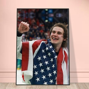 May include: A framed print featuring a smiling person draped in an American flag. The flag's red and white stripes and white stars are prominently displayed. The person is celebrating with a raised fist, set against a blurred background.