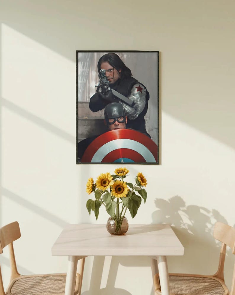 May include: A framed print featuring two characters from a superhero movie. One is aiming a gun, the other is behind a shield. A vase of sunflowers sits on a light-colored table, with two chairs on either side.